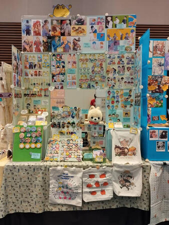 A green & blue booth with merchandise of all sorts of fandom from anime, manga, tv series and etc.
